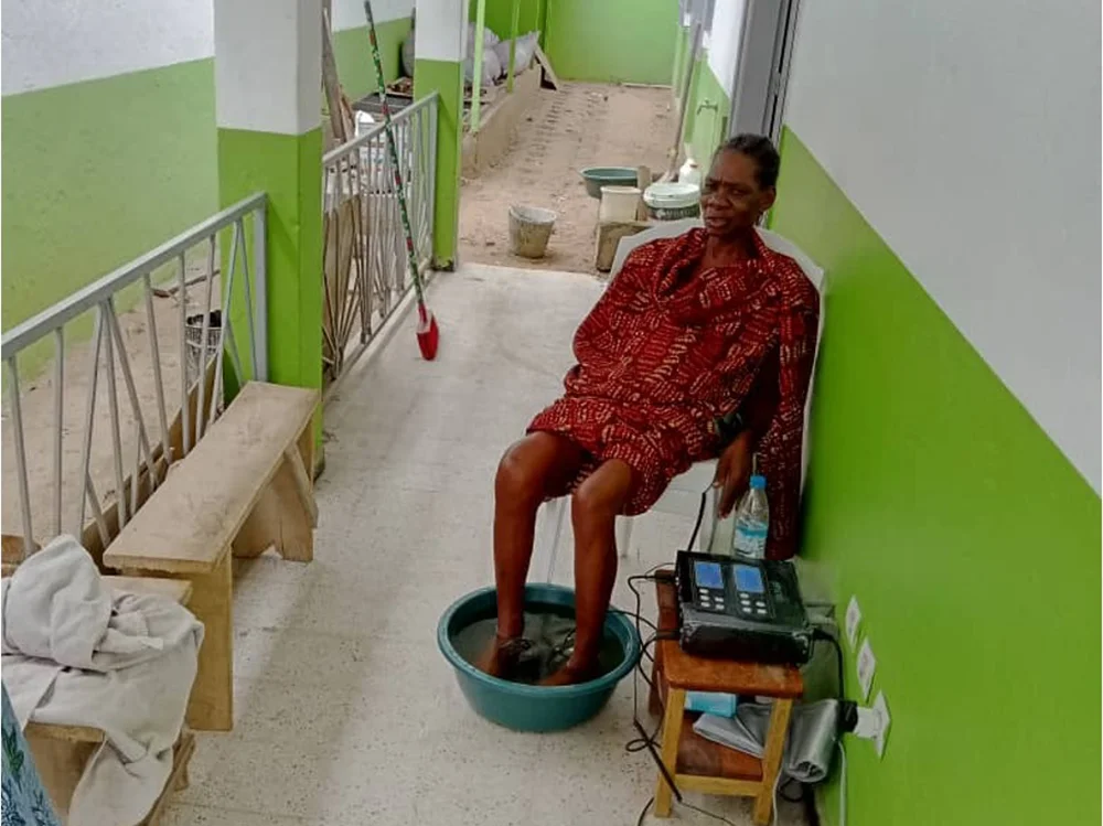 Eine Frau in Côte d'Ivoire (Elfenbeinküste) sitzt auf einer Terrasse und hat die Füsse in einem Fussbad.